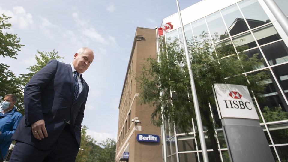 Erin O'Toole passant devant des drapeaux du Canada et du Québec ainsi que des enseignes de HSBC et de Berlitz.