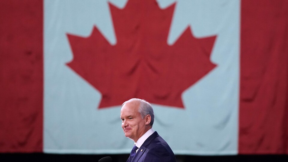 Erin O'Toole sourit à ses partisans, devant un immense drapeau du Canada.