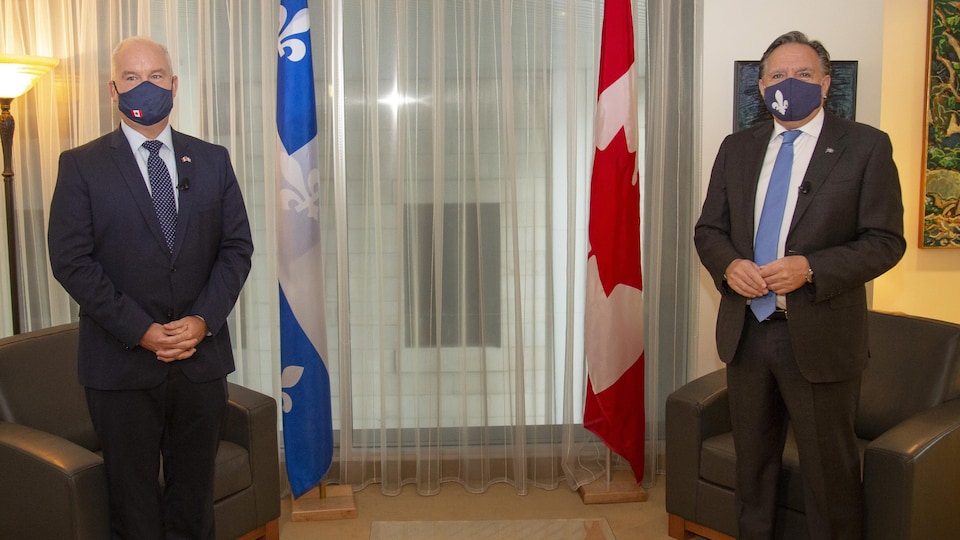 Erin O'Toole et François Legault debout et portant un masque avec un drapeau du Canada et du Québec en arrière-plan.