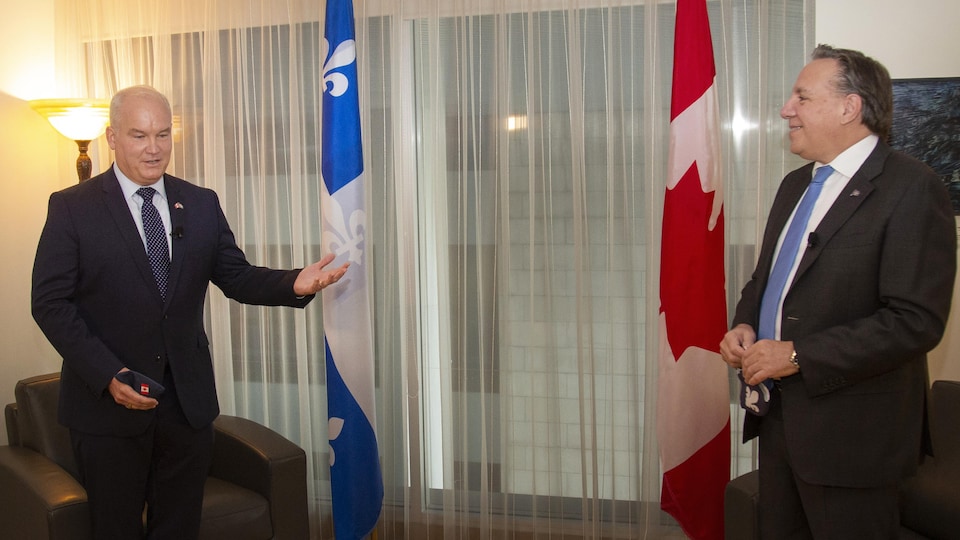 Erin O'Toole et François Legault debout avec un drapeau du Canada et du Québec en arrière-plan.