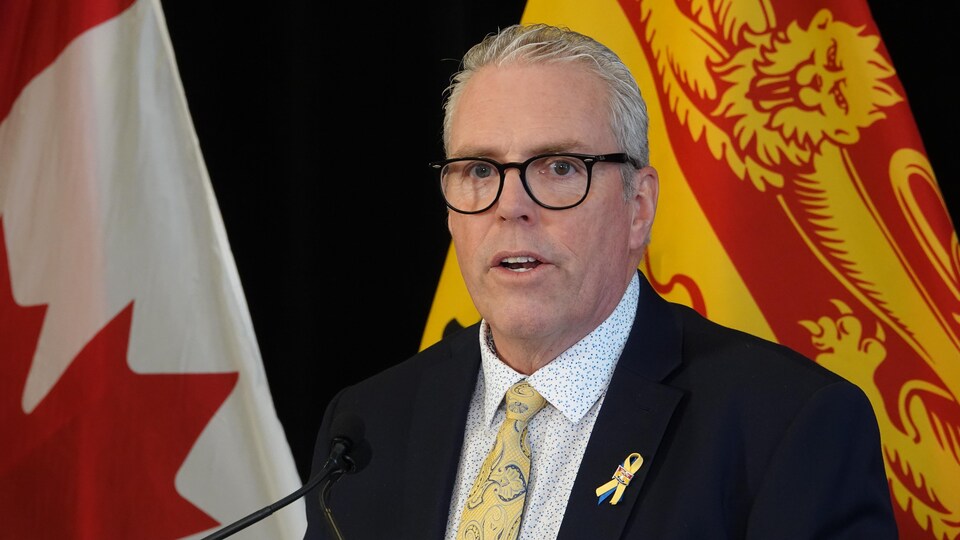 Ernie Steeves devant des drapeaux du Canada et du Nouveau-Brunswick.