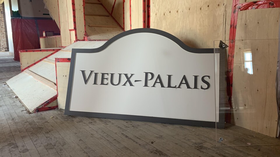 Wooden poster indicating Vieux-Palais, placed on a wooden floor, in a place under renovation.
