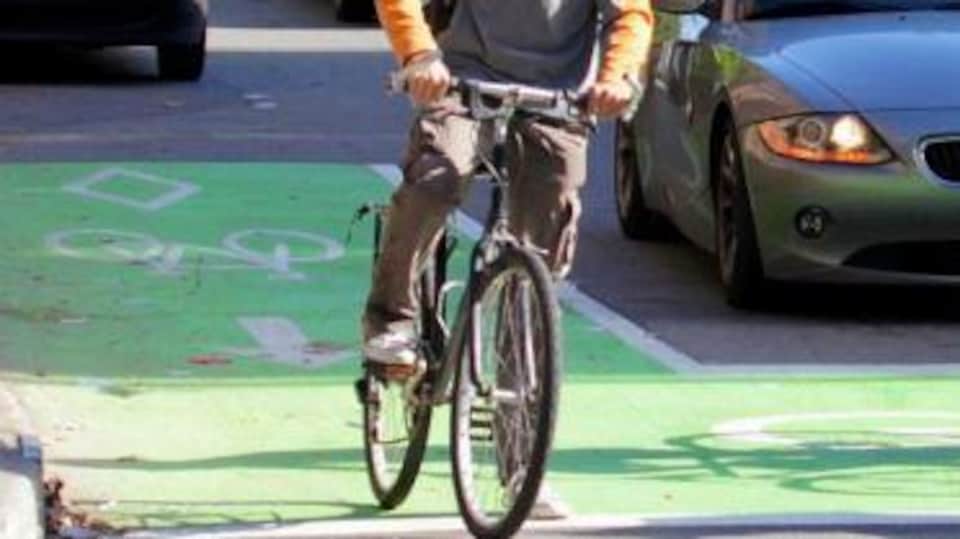 Sas de vélo à Montréal, un espace marqué en vert où l'on voit un cycliste arrêté, avec derrière lui une voiture arrêtée à une intersection.