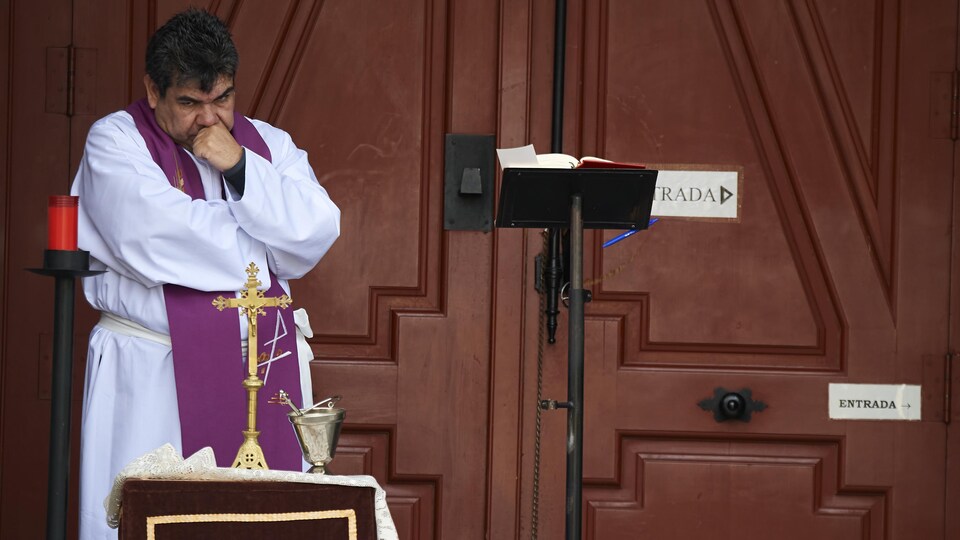 Un prêtre se tient la tête avec le point gauche, visiblement découragé.