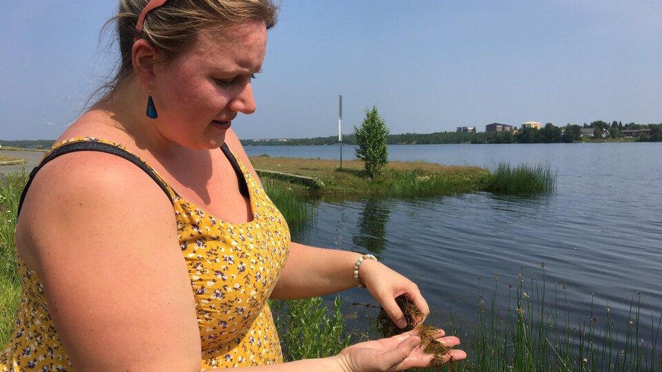 Une femme tient un espèce envahissante exotiques dans ses mains près d'un lac.