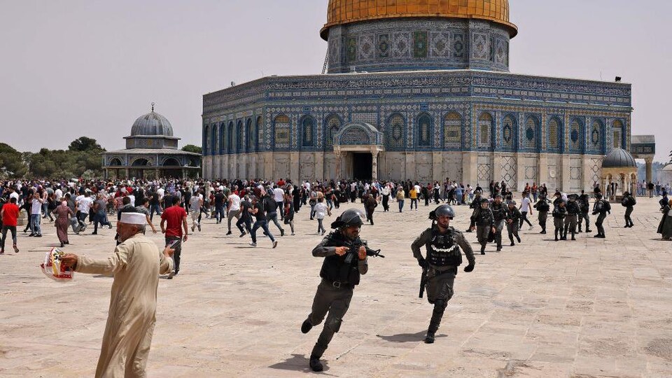 Des policiers armées et des civils courent dans tous les sens devant une immense mosquée.