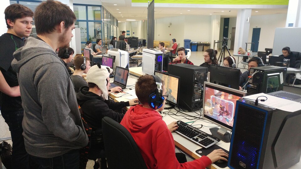 Un entraîneur derrière des joueurs de sport électronique de l'équipe Les Capitaines du Cegep de Matane jouant sur leur ordinateur dans une salle de l'école.