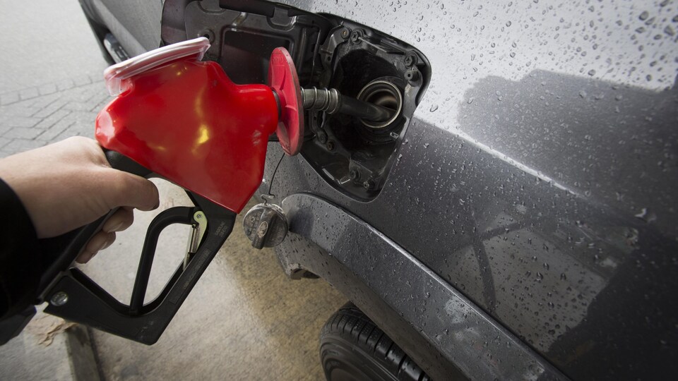 Une personne met de l'essence dans son véhicule, à une station-service.