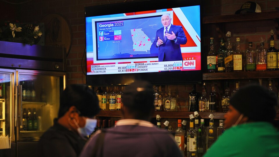 Des gens sont assis à un bar où une télé présente les résultats des courses au Sénat.