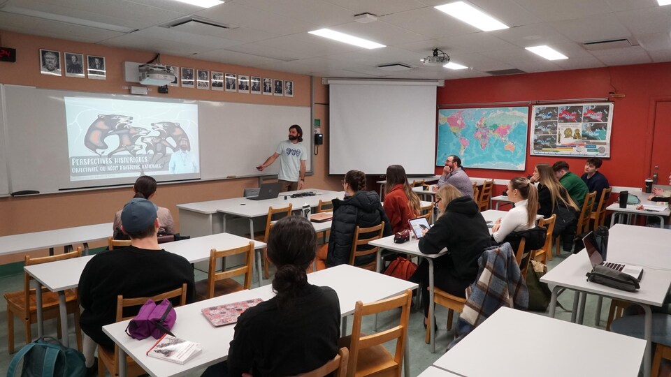 Un homme enseigne devant une classe de dix étudiants.