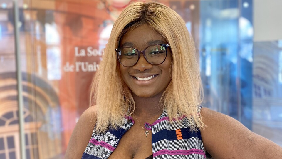 Marie Paule Ehoussou sourit devant une affiche de l'Université de Saint-Boniface. 