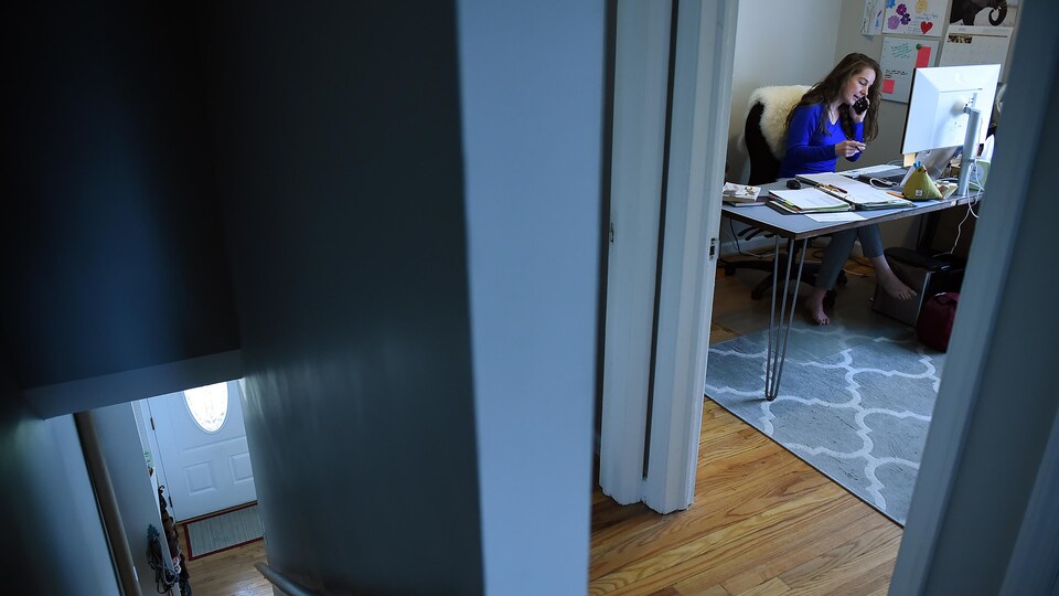 Une étudiante dans une chambre devant un ordinateur parle au téléphone.
