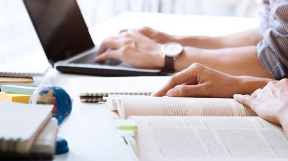 Des étudiants devant un ordinateur et un livre ouvert