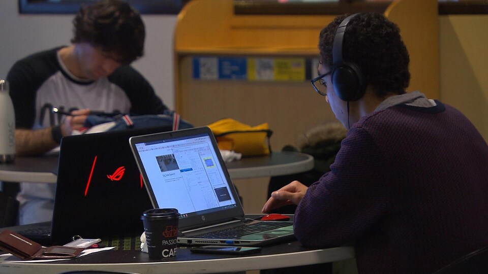 Un étudiant assis à une table travaille sur son ordinateur.