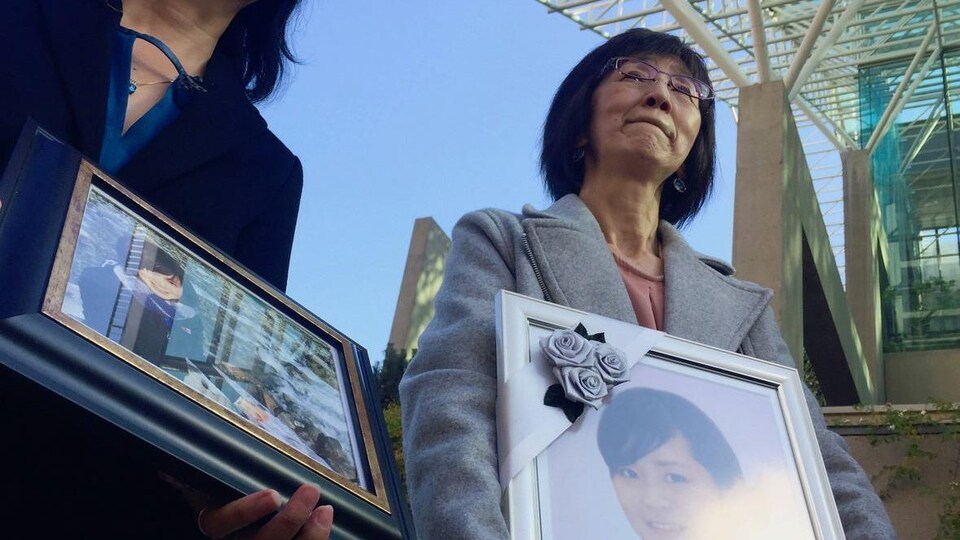 Une femme tient un cadre avec une photo, devant le Palais de Justice.