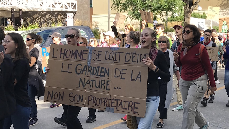 Des manifestants pour le climat avec une pancarte sur lequel il est écrit L'homme se doit d'être le gardien de la nature... non son propriétaire.