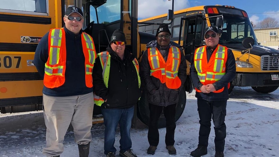 Quatre hommes souriants debout devant des autobus scolaires