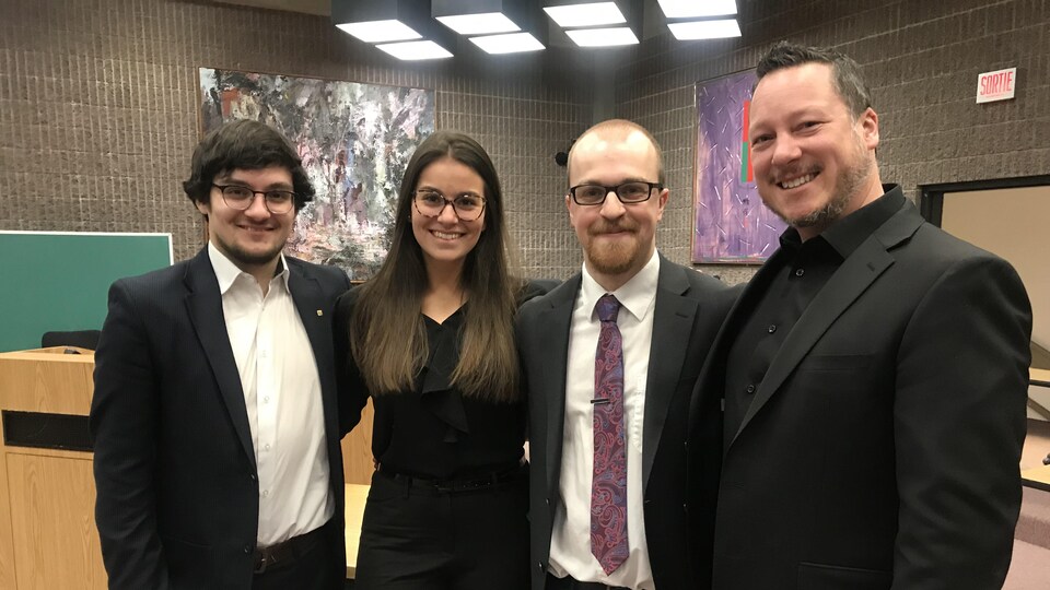 Trois étudiants en droit et leur enseignant (à droite) se penchent sur un projet de loi pour contrer l’obsolescence programmée. Ils se tiennent debout dans une salle de classe.