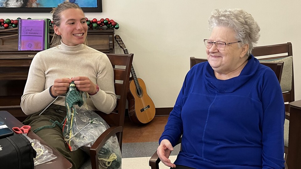 Une jeune femme rit, en tricotant, avec une femme âgée. 