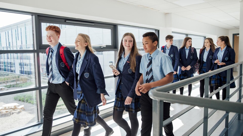 Des étudiants du secondaire marchent dans un corridor d'école.