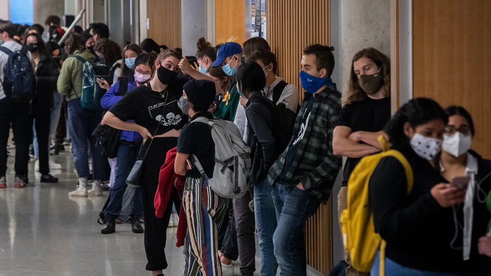 Des étudiants masqués forment une file d'attente dans les couloirs de l'université.