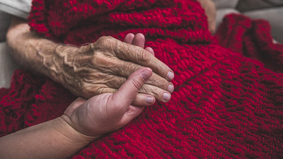 Une infirmière tient la main d'un patient âgé.