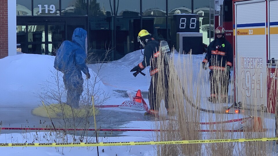 Un homme muni d'une combinaison spéciale et deux pompiers s'affairent devant la polyvalente Le Carrefour.