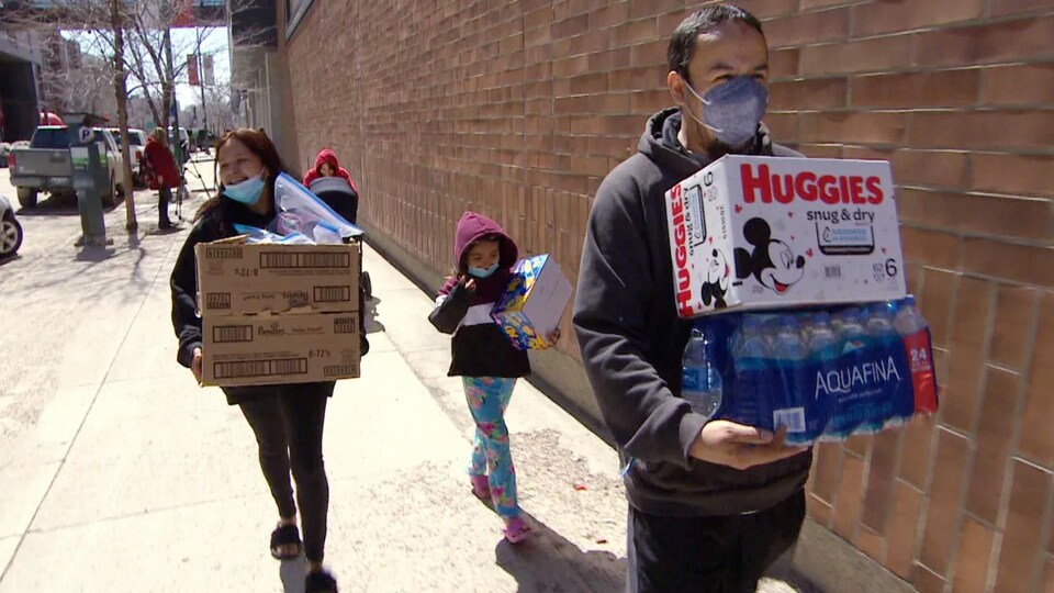 Une famille transporte des bouteilles d'eau, des couches et des boîtes sur un trottoir de Winnipeg, le 12 mai 2022.
