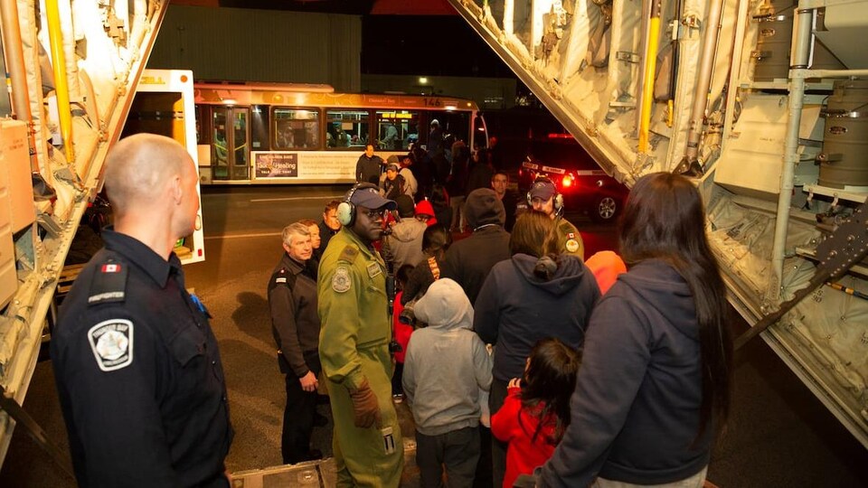 Des personnes sortent d'un avion pour se diriger vers un autobus, la nuit, en présence de militaires.
