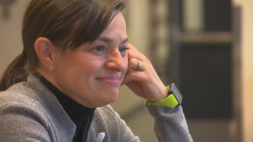 Une femme souriante avec la tête appuyée sur sa main gauche.