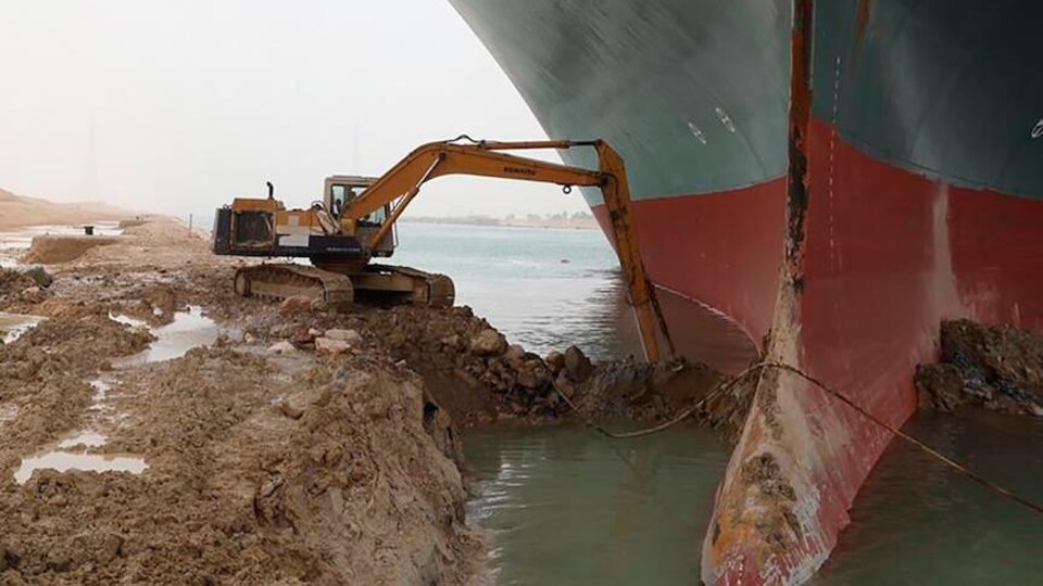 Une excavatrice tente de libérer un gigantesque navire pris au piège. 