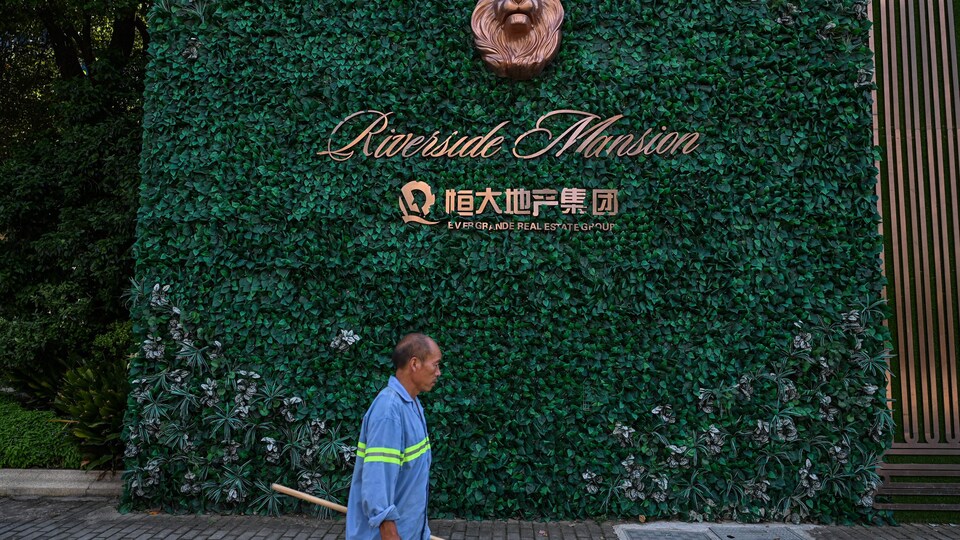 Un homme marche devant un mur végétal, près d'un édifice appartenant à Evergrande.