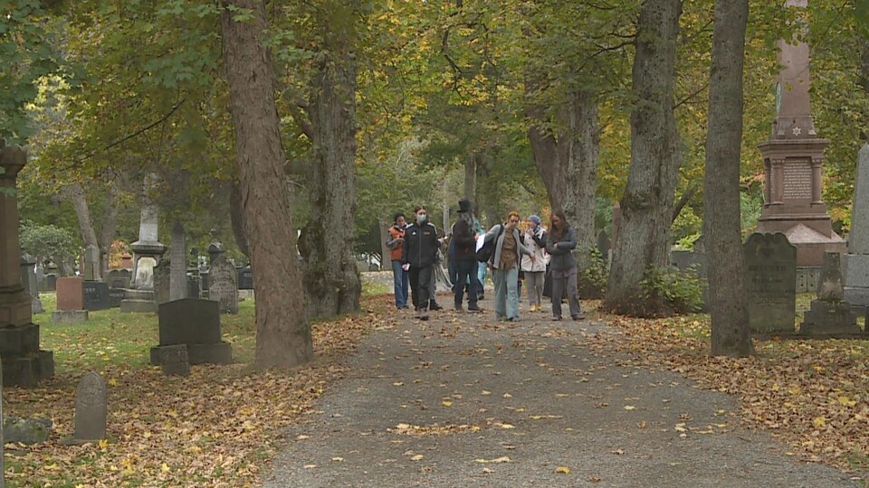 Des personnes marchent dans une allée dans un cimetière, entre des pierres tombales