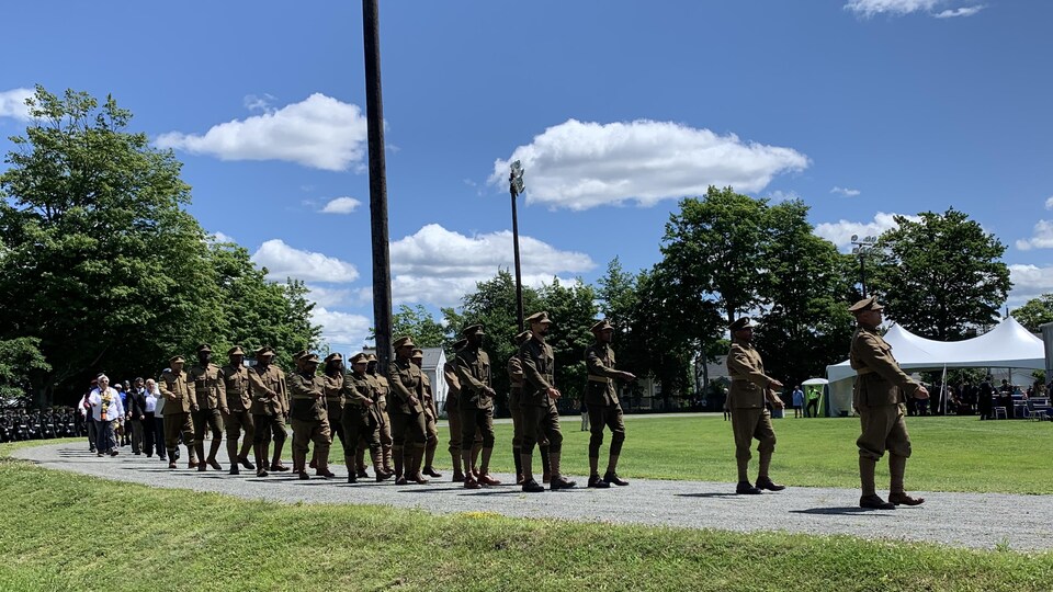 Des militaires noirs en uniforme défilent en rang dans un parc sur un chemin de gravier.