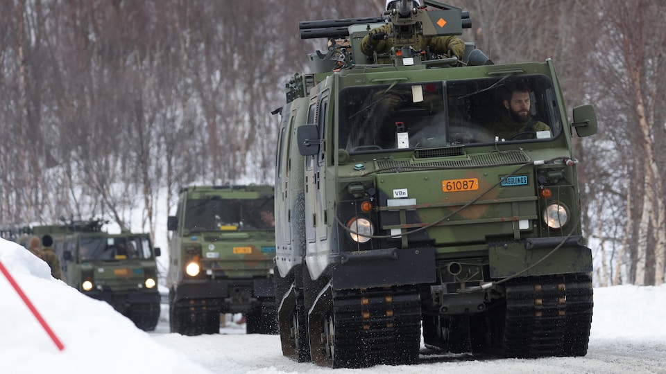 Des camions militaires circulent sur une voie enneigée.  