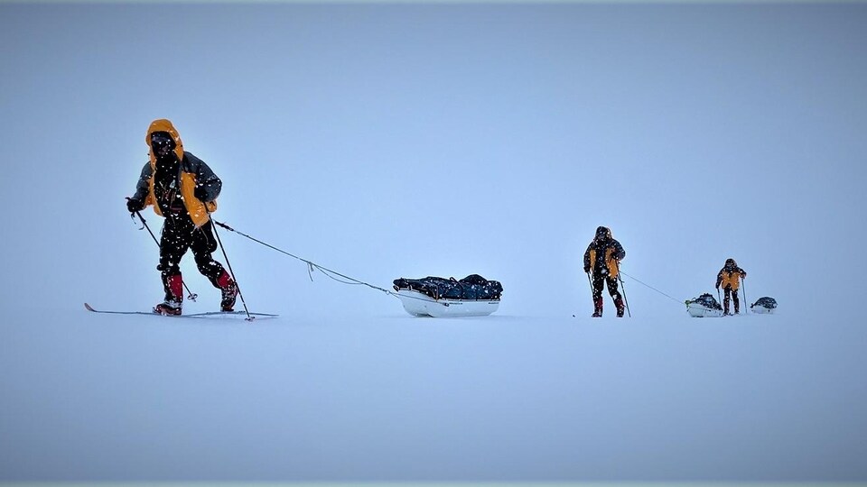 Trois hommes en ski de fond dans une tempête de neige.