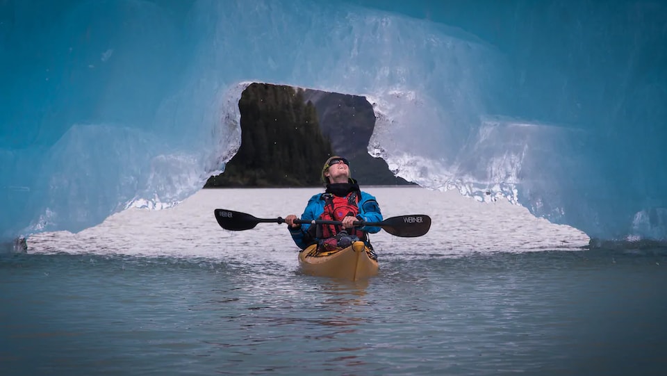 Un homme sur un kayak la tête versée vers l'arrière pour regarder la glace au-dessus de lui.