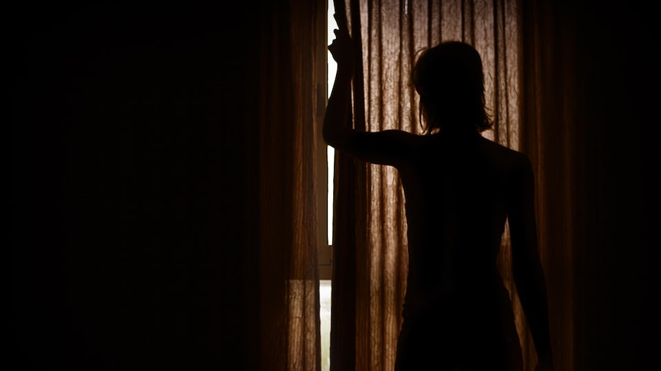Silhouette d'une femme qui ouvre les rideaux d'une chambre d'hôtel.