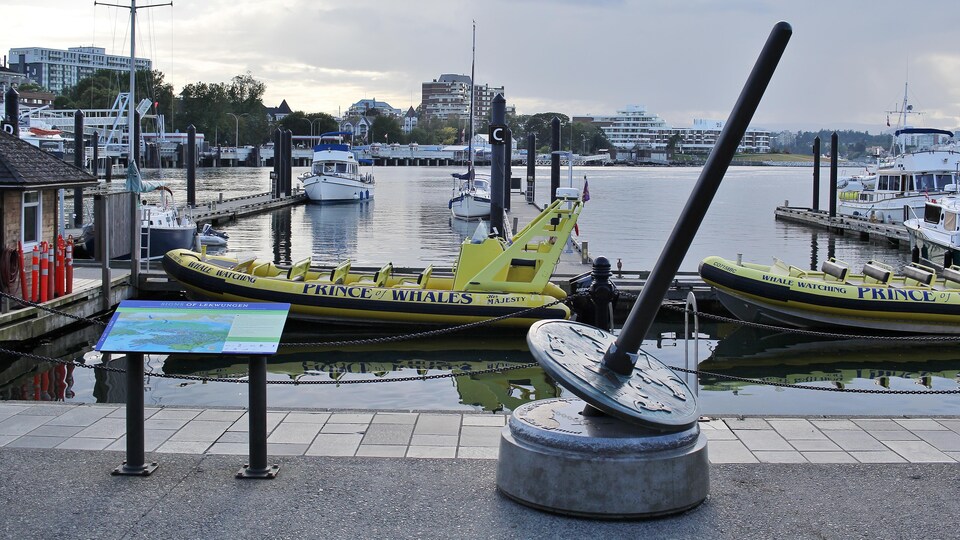 Une sculpture en forme de fusaïole sur le quai devant des bateaux dans le port de Victoria.