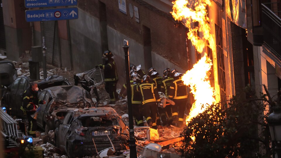 Des pompiers transportent une civière devant la façade l'immeuble détruit.