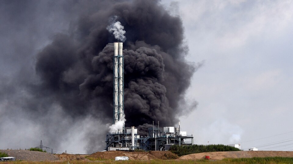 De la fumée noire s'élève dans le ciel autour de la cheminée d'un incinérateur.