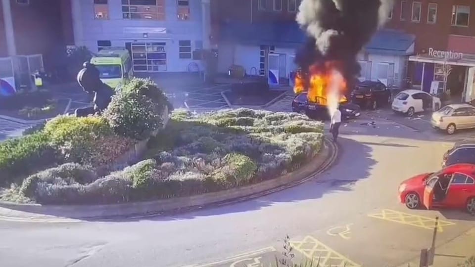 Un homme utilise un extincteur pour éteindre un véhicule en feu dans un rond-point, près d'un hôpital. 
