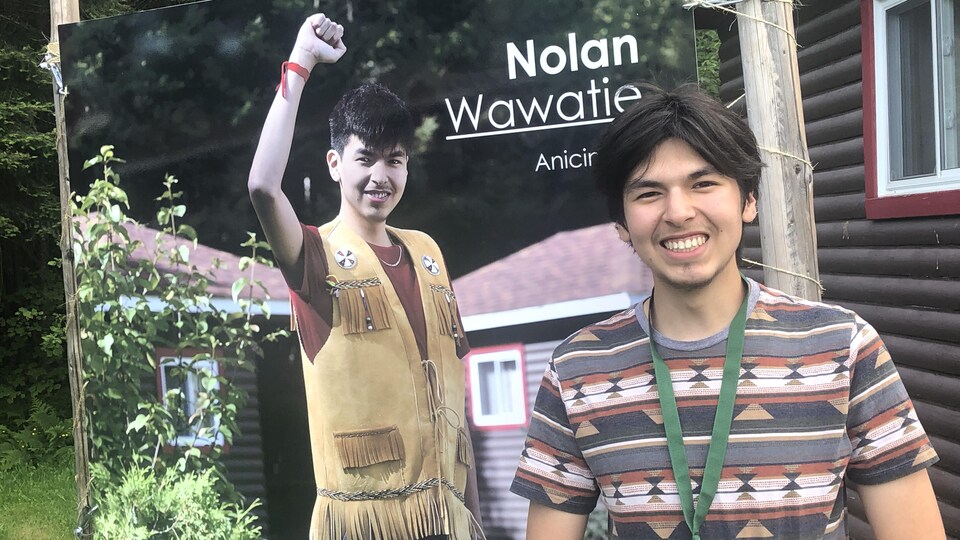 Nolan Wawatie pose devant son affiche dans l'exposition.