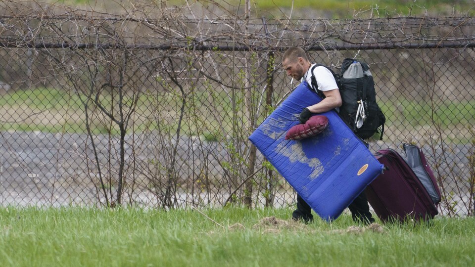 Un homme lourdement chargé marche sur l'herbe.