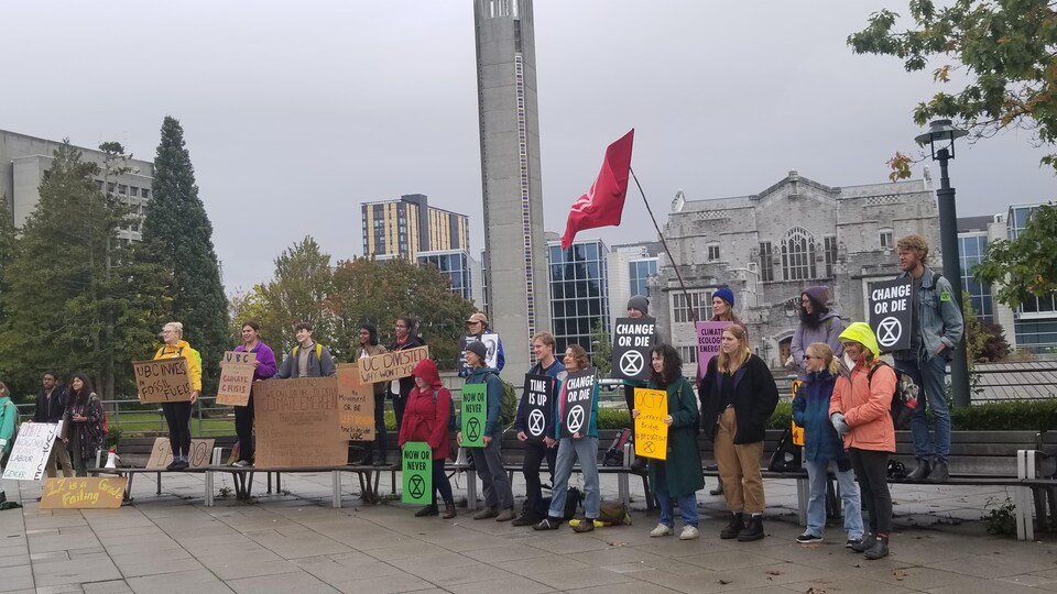 Des jeunes en ligne tiennent des affiches, ils sont devant un bâtiment universitaire.