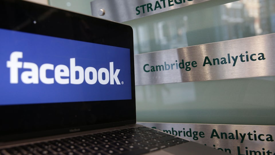 Un ordinateur portable montrant le logo de Facebook est posé à côté d'une plaque indiquant les bureaux de Cambridge Analytica, à Londres, le 21 mars 2018.