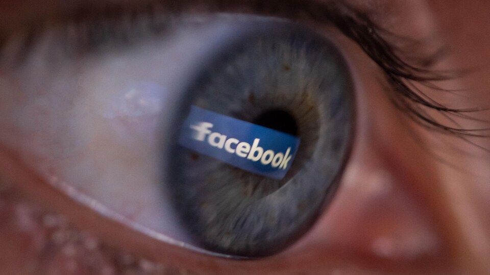 Un œil, vu de proche, avec la réflexion du logo de Facebook.