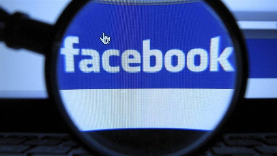 Une loupe grossit le logo de Facebook qui s'affiche sur un écran d'ordinateur.