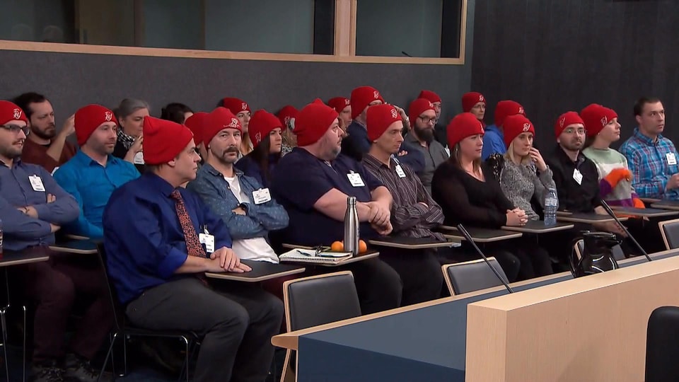 Des manifestants vêtus de tuques rouges sont assis dans la salle.