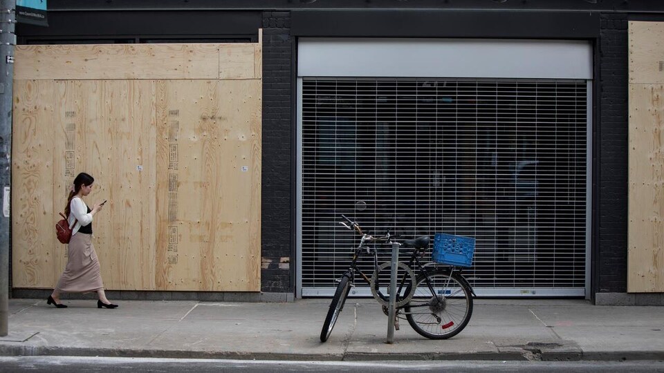 Une femme passe devant la façade d'un commerce placardé
